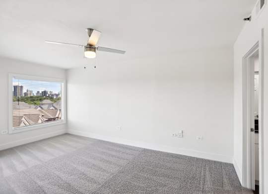 A room with a ceiling fan and a window overlooking a cityscape.
