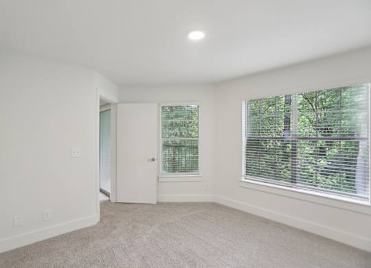A bedroom with a carpeted floor and a window with blinds.