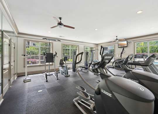 A gym with treadmills, elliptical machines, other equipment,  and a fan.