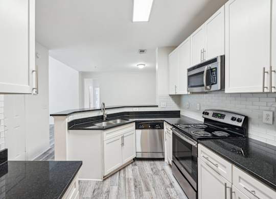 A kitchen with black countertops, stainless steel appliances, and white cabinets.