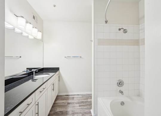 A white bathroom with a black counter top and a white bathtub.