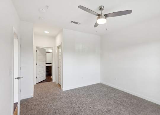 A bedroom with a ceiling fan and carpeted floor.