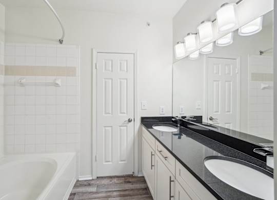 Bathroom with double sinks, black countertop, white shower and tub.