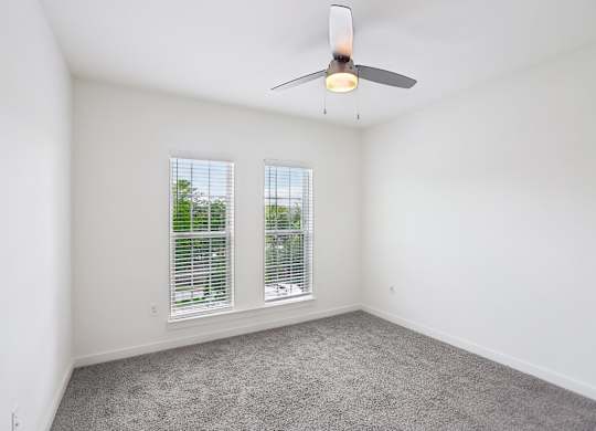 A bedroom with a ceiling fan and two windows.