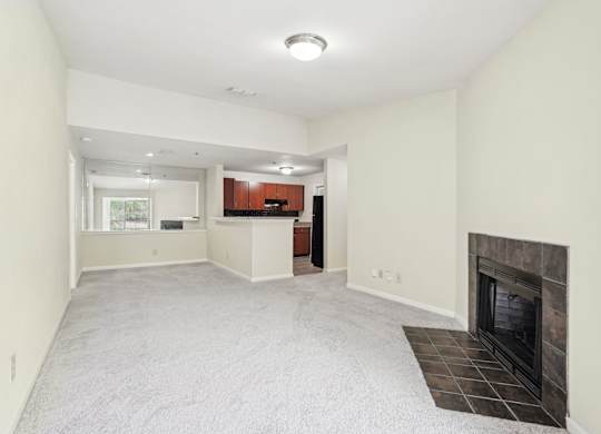 A spacious living room with a fireplace and a kitchen in the background.