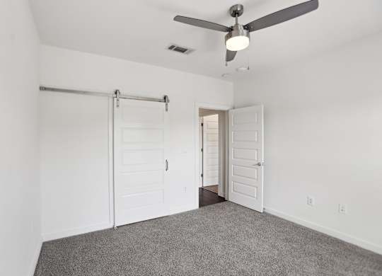 A bedroom with a ceiling fan and barn door closet.