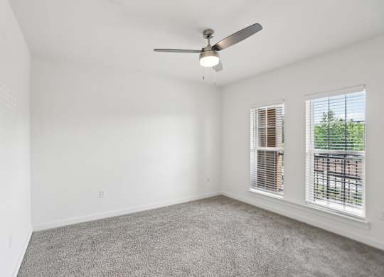 A large bedroom with a ceiling fan, windows, and carpeted floor.