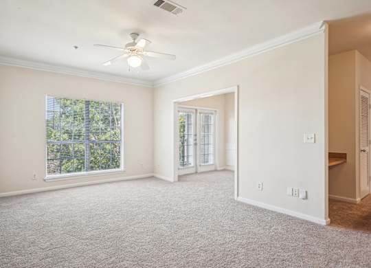 A spacious living room with a ceiling fan, carpeted floor and windows.