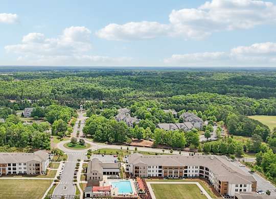 aerial view of the apartment complex with the pool ad many trees in view with beautiful skies