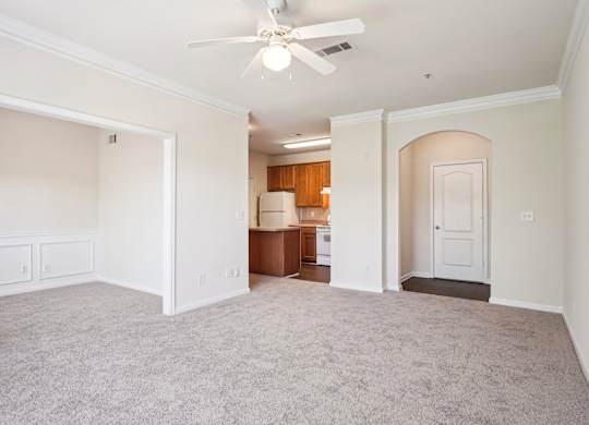 A spacious  living room with a ceiling fan and carpeted floor.