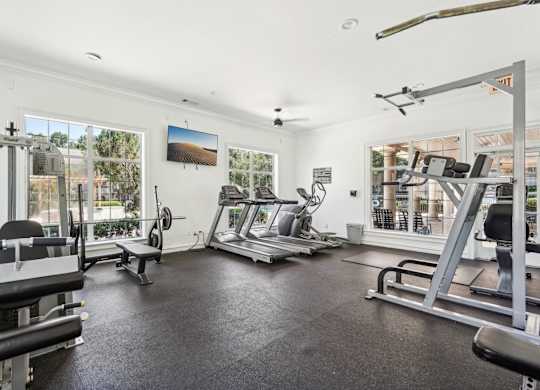 A spacious gym with various exercise equipment and a view of the outdoors through the windows.