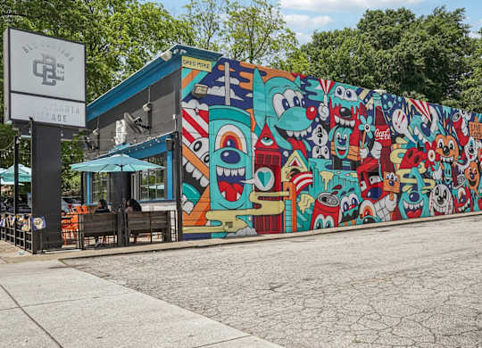 East Atlanta Village: A mural of by the famous Greg Mike with cartoon characters is displayed on a wall next to a building.