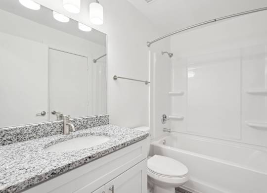 A bathroom with a granite countertop and a white tub and shower