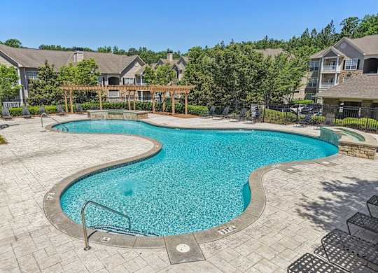 A large outdoor swimming pool surrounded by a wooden fence and residential houses.