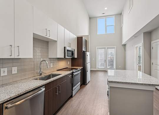 A modern kitchen with a large island and stainless steel appliances. A large bedroom with a ceiling fan and a window s. a large, high ceiling, apartment that has two floors, is a modern loft, and in atlanta