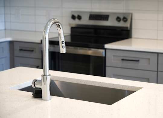 A kitchen sink with a chrome faucet. and stain gray and white cabinets