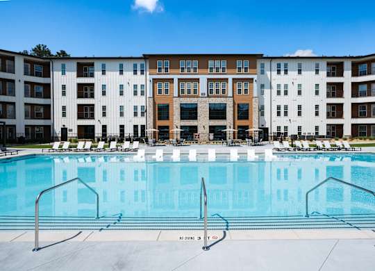 A large swimming pool in front of a multi-story apartment building.