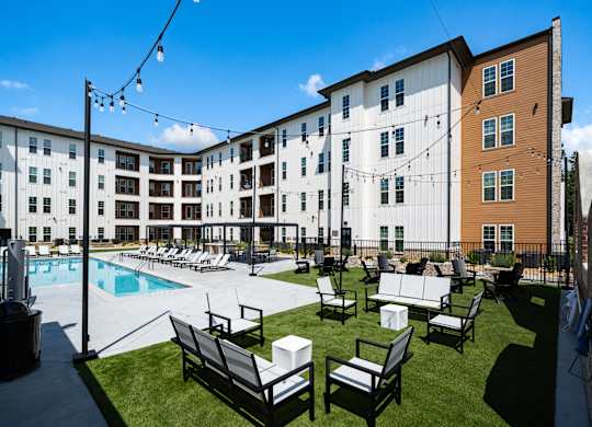 A sunny day at the poolside with chairs and a building in the background.