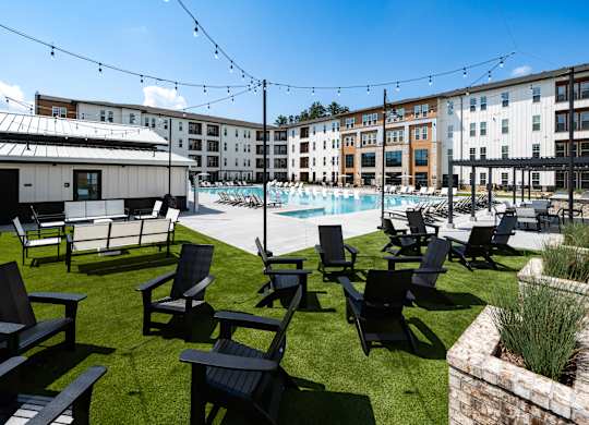 A sunny day at the poolside with chairs and a building in the background.