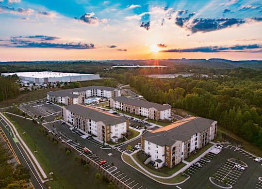 A sunset view of a large apartment complex with a parking lot in the foreground.