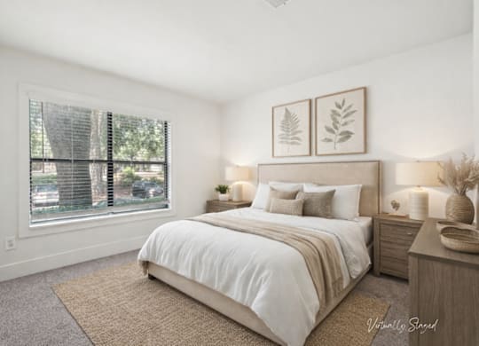 A bedroom with a large bed, a window with blinds, and a wall-mounted light fixture.