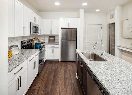 A large kitchen with a granite countertop and stainless steel appliances with white cabinets