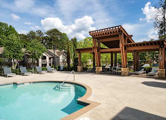 A pool with a wooden pergola and lounge chairs.