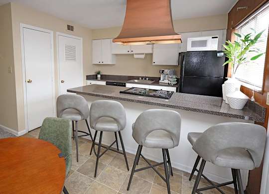 A kitchen with a black fridge, white cabinets, and a brown hood.