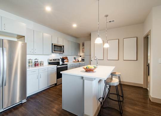 a kitchen with white cabinets and a white island with two stools at Parkside at Littleton Village, Littleton, CO