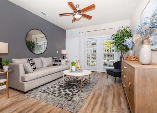 A living room with a beige couch, a round mirror, a coffee table, and a ceiling fan.