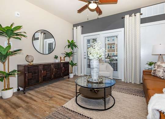 A living room with curtains, a glass coffee table and a brown couch.