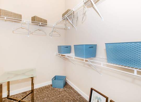 A room with a white wall and a shelf with clothes hangers and baskets.