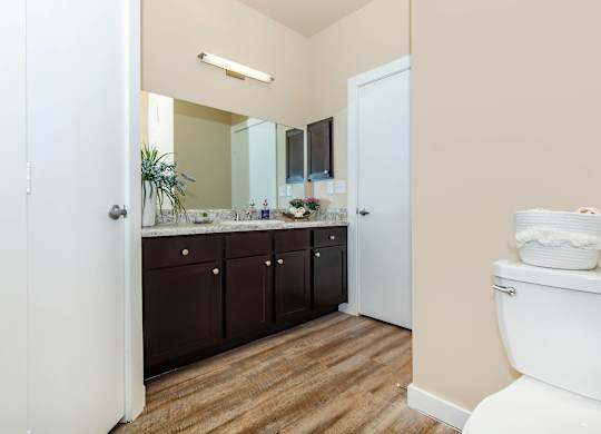 A white toilet sits in a bathroom with wooden floors and brown cabinets.