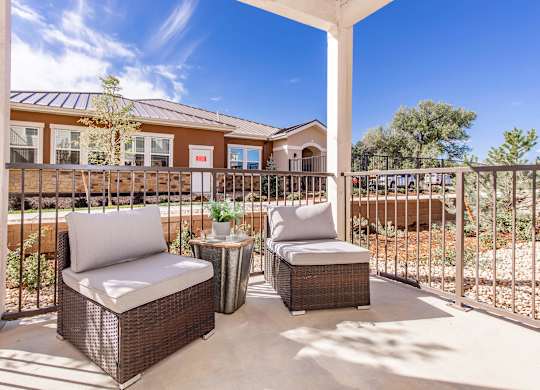 Two wicker chairs are on a patio with a building in the background.