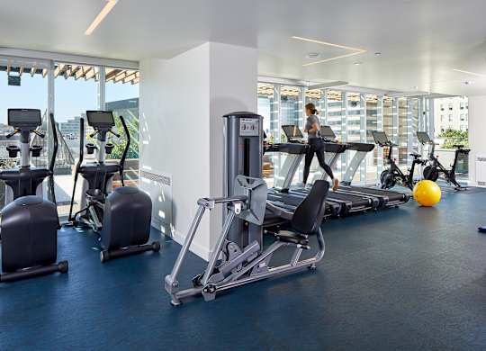 A gym with a row of treadmills and a woman working out.