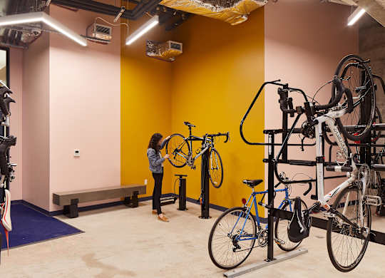 A woman is standing in a room with a yellow wall and several bicycles.