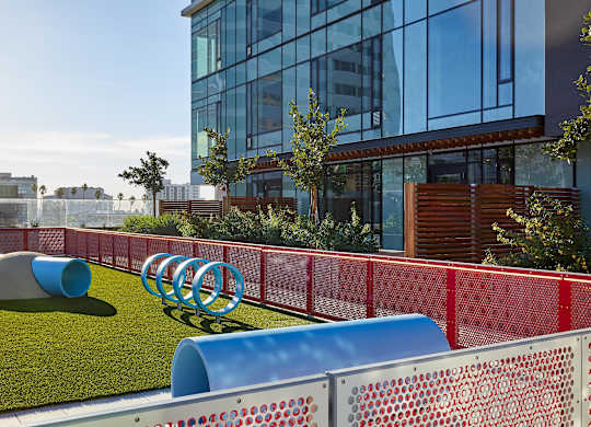 A playground with a red fence and blue and grey slides.