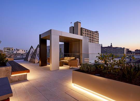 A modern building with a unique design is illuminated by lights at dusk.