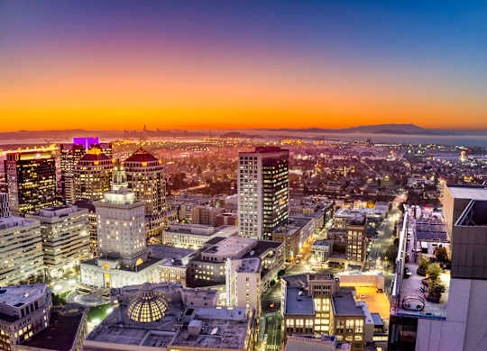 A cityscape at dusk with buildings illuminated against a twilight sky.