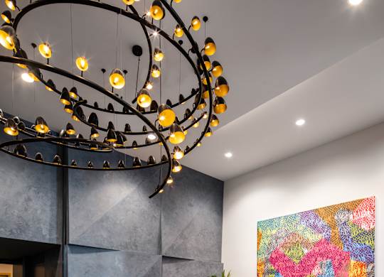 A modern living room with a large abstract painting on the wall and a unique chandelier.