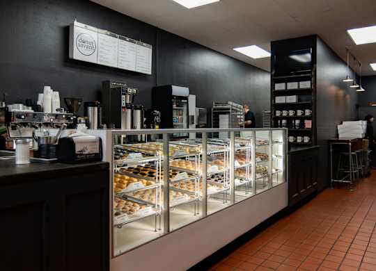 A bakery with a display case filled with pastries and a counter with coffee cups.
