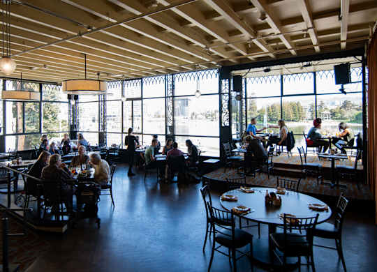 A group of people are sitting at tables in a restaurant with a view of the outside.