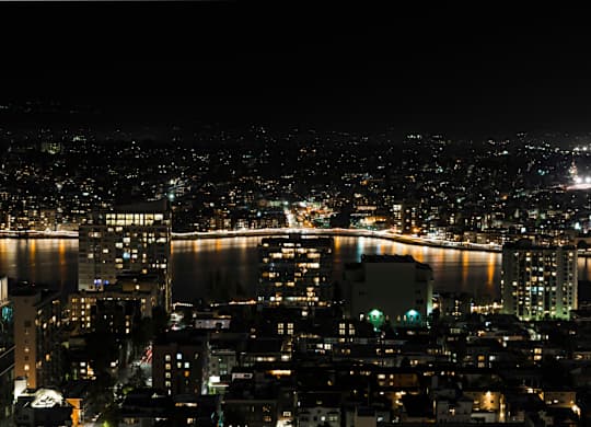 A cityscape at night with lights from buildings and a body of water.