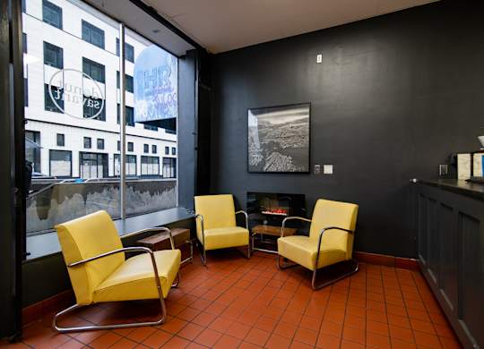 A room with four yellow chairs and a fireplace, with black walls.