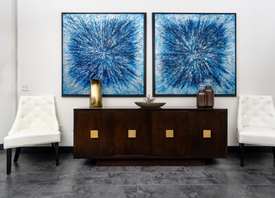 two large abstract paintings hanging on a wall above a wooden cabinet