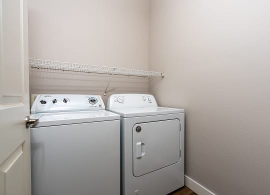 a washer and dryer in the corner of a room with a shelf above