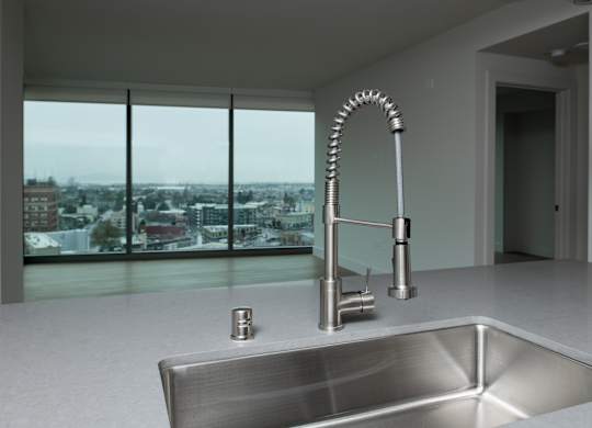 A modern kitchen with a stainless steel sink and a large window overlooking a cityscape.