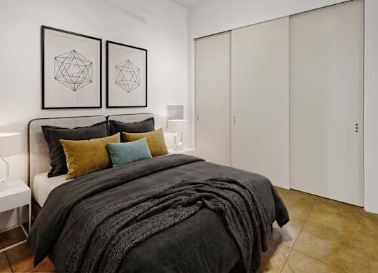 A bedroom with a bed, two pillows, a nightstand, and two framed geometric artworks on the wall.