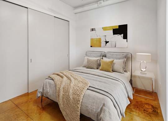 A bedroom with a bed, a blanket, a lamp, and a painting on the wall.