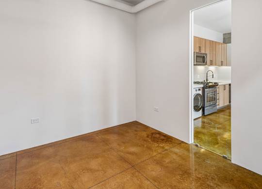 A kitchen with white walls and a brown floor is visible through an open door.